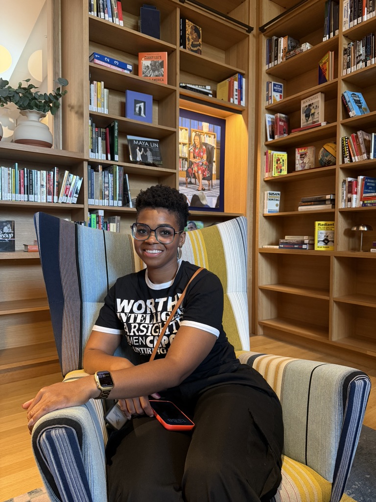 Lo smiling in a striped armchair in front of library bookshelves